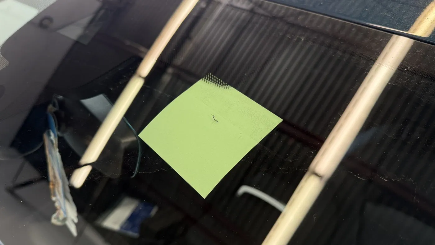 Rock chip on a windshield marked with a green sticky note for repair assessment